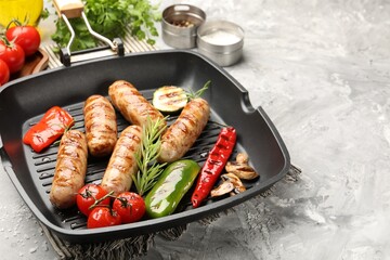 Pan with grilled sausages, vegetables, mushrooms and spices on gray textured table, closeup