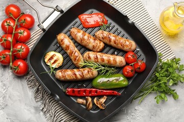 Pan with grilled sausages, vegetables, mushrooms and spices on gray textured table, flat lay
