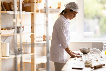 Female baker rolls dough into long sausages to be cut into pieces for baking buns