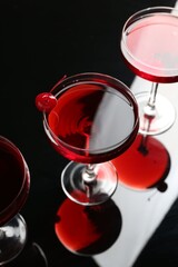 Glasses of tasty cocktails with garnish on mirror surface, above view