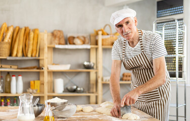 Elderly man baker cutting dough with scraper