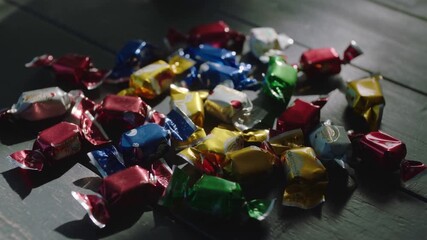Framing assorted foil-wrapped candies resting on dark wooden tabletop, highlighting color contrast - Powered by Adobe
