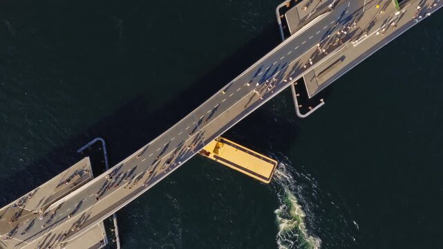 Aerial drone view of a yellow harbor bus passing under the Lille Langebro, cycling and pedestrian bridge in Copenhagen, Denmark
