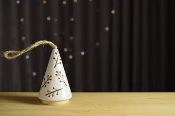 Charming decorative ceramic Christmas tree on a wooden table against the background of curtains with a garland of light bulbs