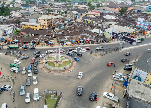 Aerial view of a bustling roundabout with a central monument, cars weaving through traffic, and buildings lining the roadsides, Owerri, Nigeria.