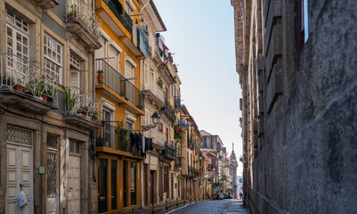 A quiet morning on a narrow cobblestone street in Porto, flanked by colorful traditional houses with wrought-iron balconies, under a clear blue sky.