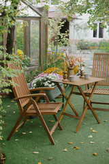Cozy exterior autumn atmosphere in garden - table and chairs, flowers, fallen leaves. Interior Backyard home with garden furniture, fall decor and plants