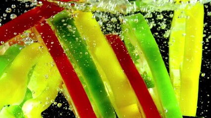 Falling Multicolored Pepper. Slices of red, yellow and green peppers fall in the water on a black background. Slow Motion - Powered by Adobe