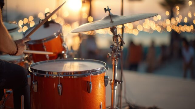 Musician playing drum kit at outdoor concert during sunset with bokeh lights. Live music performance on stage for entertainment background.