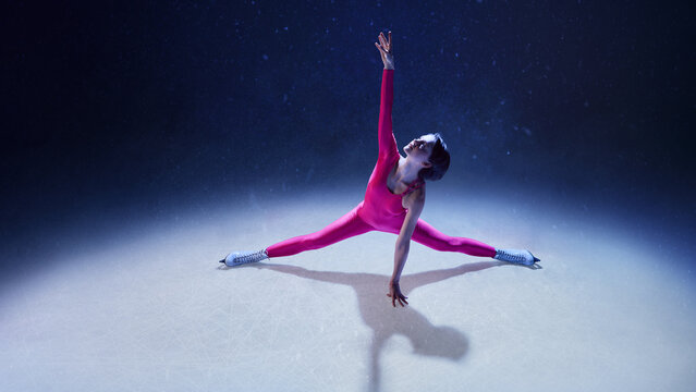 Female figure skater in pink bodysuit performing split stretch on ice with emotional precision. Concept of physical discipline, mindful energy, elegant strength, and expressive performance in motion.