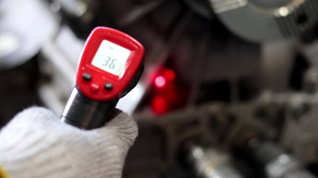 Red infrared thermometer gun showing a temperature reading of 36.3 degrees Celsius, held by a gloved hand.