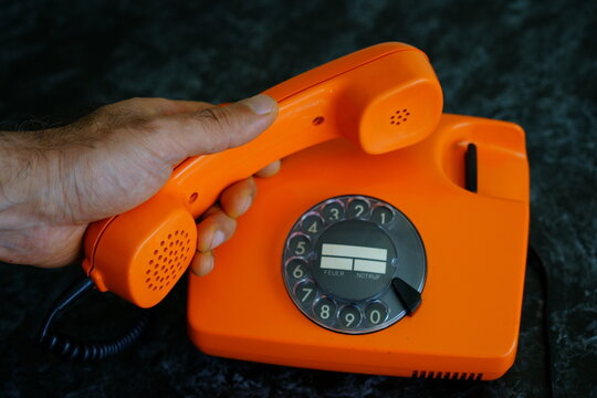 Bright orange rotary phone being lifted off the receiver on a dark surface in a cozy, retro setting