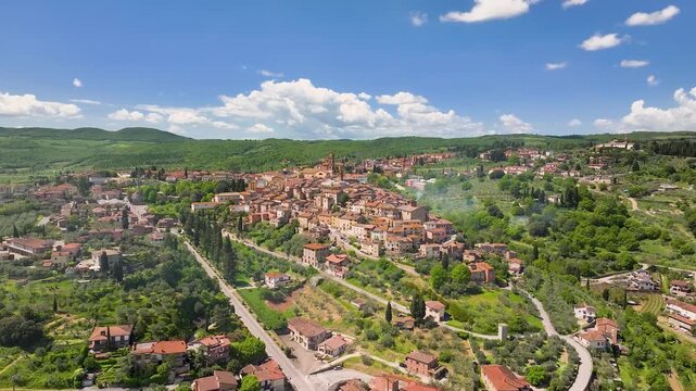 Aerial view of the vibrant Sinalunga cityscape nestled among the rolling green hills under a bright blue sky dotted with fluffy white clouds, Sinalunga, Tuscany, Italy.