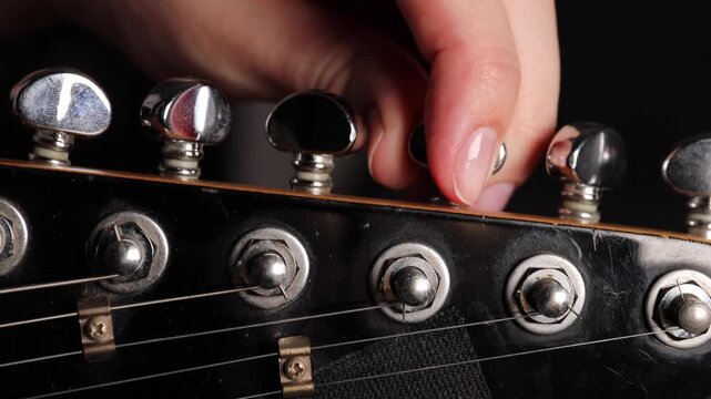 Tuning an electric guitar by adjusting tuning pegs with fingers