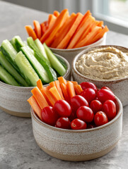 Vegetable snacks with hummus in bowls on a gray counter.