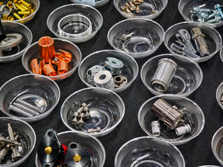 Metal components arranged in clear bowls on a black surface for display at a hardware fair or...