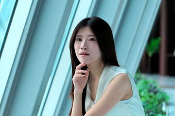 大きな窓辺で微笑む美しいアジア人女性のポートレート。癒やし、安心感、リラックスを表現し、美容、健康、ライフスタイル、明るい職場環境のイメージ素材に最適な高品質写真