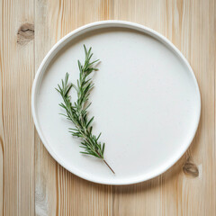 A white plate with a green herb on it. The herb is a sprig of rosemary