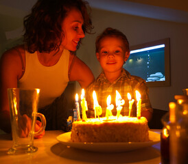 mother lights candles on her four-year-old son's birthday cake at home.