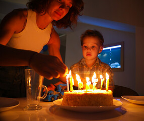 mother lights candles on her four-year-old son's birthday cake at home.
