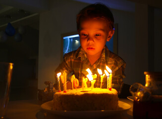 little three-year-old boy sits alone in front of a cake with candles on his birthday at home