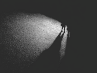 Two figures cast long shadows on rough textured surface, illuminated by a spotlight