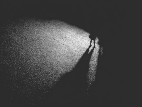 Two figures cast long shadows on rough textured surface, illuminated by a spotlight
