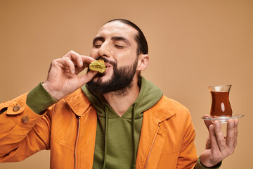 Fototapeta premium Handsome man enjoying tea and dessert in a stylish studio setting