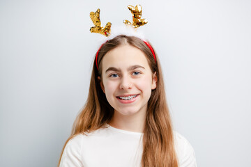 Smiling girl with sequin reindeer antlers on white background. Festive portrait for Christmas and winter celebrations.