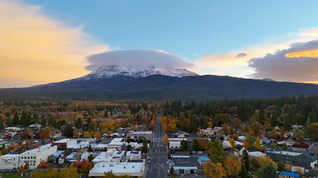Aerial view of Mount Shasta capped with a lenticular cloud, towering over a town adorned with autumn colors, Mount Shasta, California, United States.
