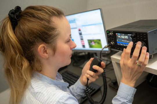 Young woman with ribbon in her hair operating amateur radio on shortwave, holding a microphone and representing YLs and females in STEM and technology fields