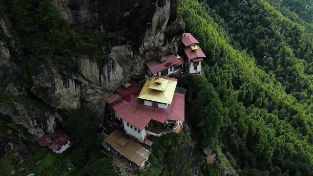 Aerial view of the Tigers Nest Temple clinging dramatically to a cliffside, a tapestry of red roofs and golden spires amidst the lush Bhutanese landscape, Paro, Bhutan.