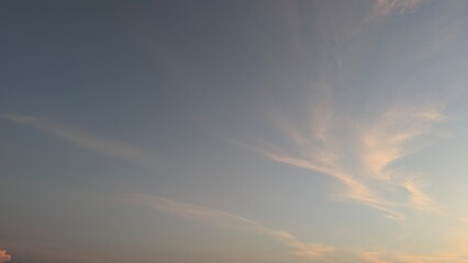 A calm dawn sky featuring delicate, wispy cirrus clouds streaked with soft peach and pink light,...