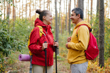 A couple smiles at each other while hiking through a colorful forest in autumn, enjoying each other's company amid nature