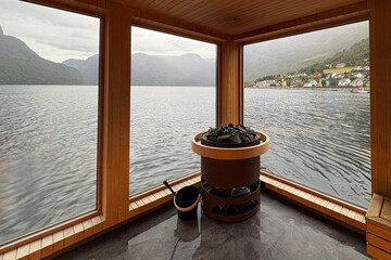 Naklejka na ściany i meble Interior shot of modern wooden sauna overlooking misty fjord through large windows.