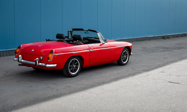 red MG MGB roadster on a street near blue wall. Rear three quarter view of old 1960s open top british sports car. Kyiv, Ukraine - September 30 2024