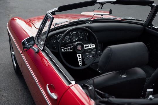 Interior of red MGB classic roadster. 1960s MG sports car with black leather interior, asphalt road in the background. Kyiv, Ukraine - September 30 2024