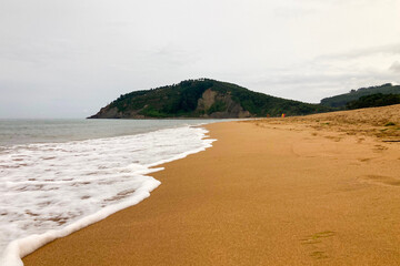 Rodiles Beach in Villaviciosa, Spain, under cloudy weather with soft waves, wet sand, and a calm, moody coastal atmosphere.