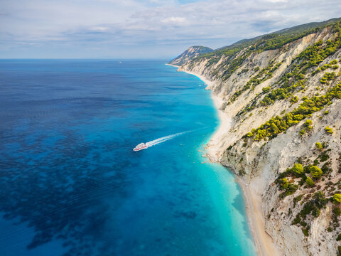 Aerial view of a boat cruising along the turquoise waters meeting the white cliffs of Porto Katsiki beach, Lefkada, Greece.