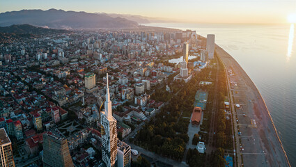 Aerial view of Batumi, Georgia with modern skyscrapers, coastline, and mountains at sunset.