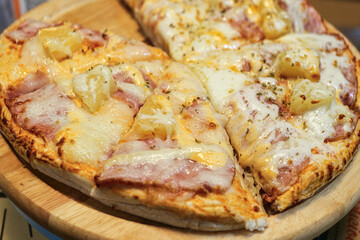 Close-up of Hawaiian Pizza slices (ham, pineapple, melted cheese, cream sauce) on a wooden tray. A popular, savory-sweet Thai street food item, dusted with oregano.