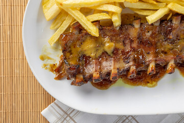 Glazed pork ribs with french fries served on white plate