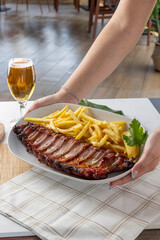 Server delivering bbq pork ribs and french fries with beer