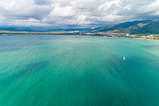 Yacht competitions in Gelendzhik Bay. Many small yachts on water. Aerial view. Caucasus Mountains in background. Children's regatta