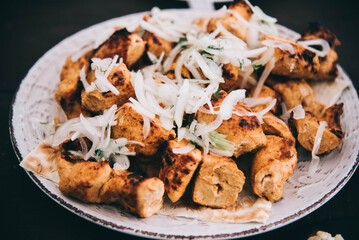 Cooked shashlik on a white plate with onions. Grilled pork with a crispy crust. Meat at a party. Grilled pork pieces close-up. 