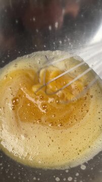 Close-up view of whisking eggs in a glass bowl. Smooth mixing motion, yellow yolks and foam forming concept of cooking, baking preparation, and homemade meal process.