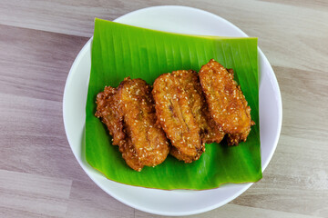 Crispy Thai fried bananas with sesame seeds served on a banana leaf in a white plate, Fried bananas is a traditional Asian snack with sweet, crunchy texture. Top view shot