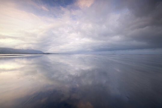 View of a serene expanse where the sky kisses the earth, reflections blurring the line between reality and dream in Dyrholaey, Iceland.