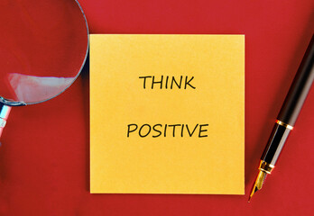 A yellow sticky note with THINK POSITIVE written on it sits next to a fountain pen and a magnifying...