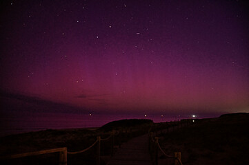 View of a dark path leading to the beach under a vibrant magenta and violet sky speckled with stars, casting a serene glow over the landscape, Seignosse, Nouvelle-Aquitaine, France.